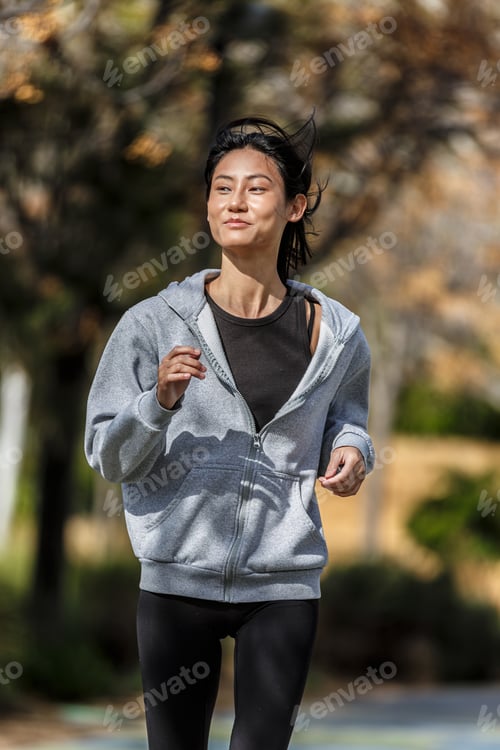 Preview: Young Asian woman jogging in the park during daytime workout session