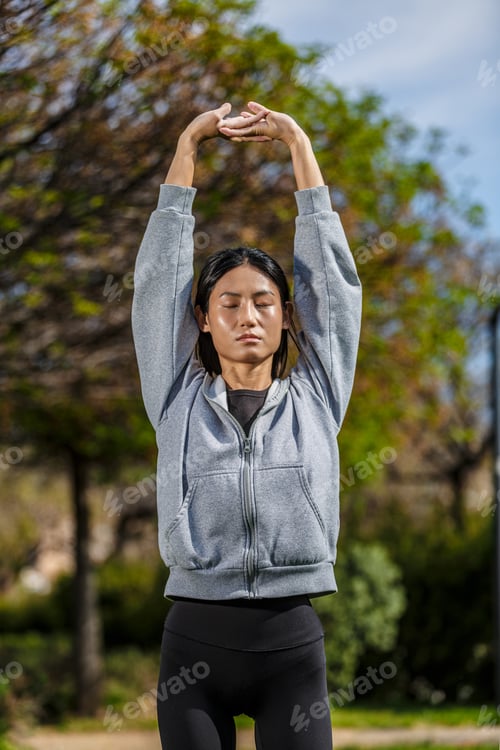 Preview: Young Asian woman stretches in a park in Spain during a sunny day