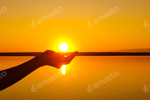 Preview: Human hand holding sun at serene sunset over lake