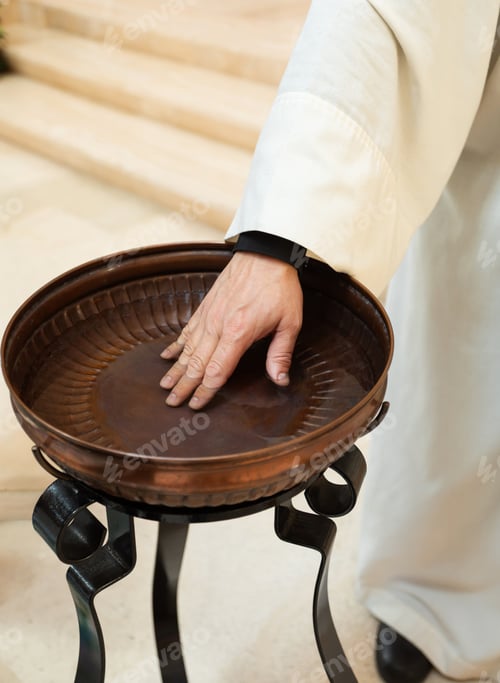 Preview: Priest's hand touching water in baptismal font