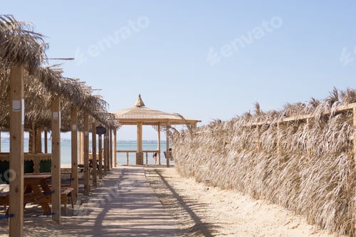Preview: Thatched roofs and wooden boardwalk on a sandy beach leading to the sea. Relaxing tropical resort se