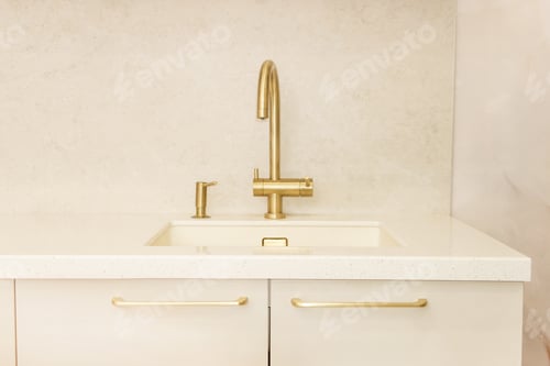 Preview: Gold faucet and basin in modern beige kitchen interior. Minimalist sink area with luxury metal hardw