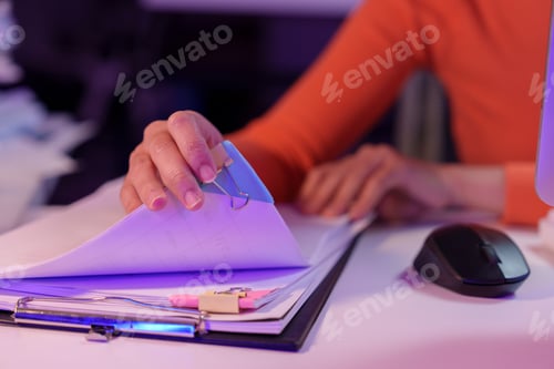 Preview: Person in an office setting organizes documents with a binder clip on a desk. The scene includes a m