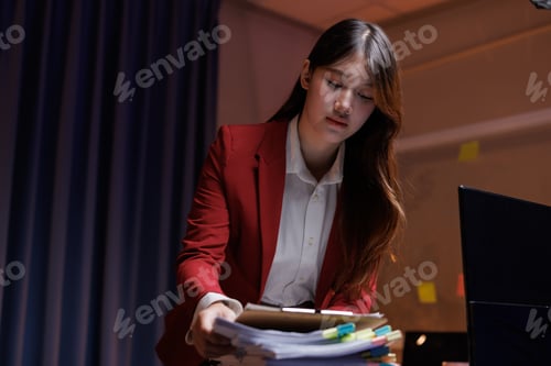 Preview: Young businesswoman working late organizing documents in office