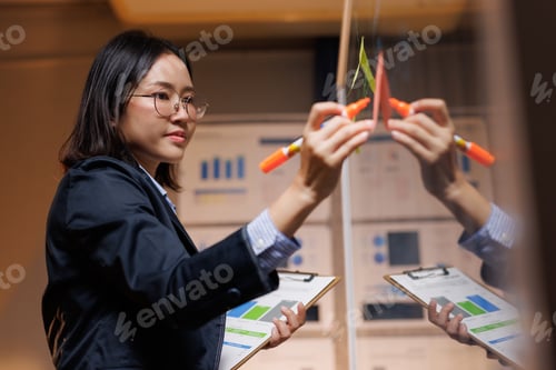 Preview: Asian businesswoman writing strategy on glass board at night