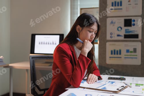 Preview: Young businesswoman thinking while analyzing financial data charts