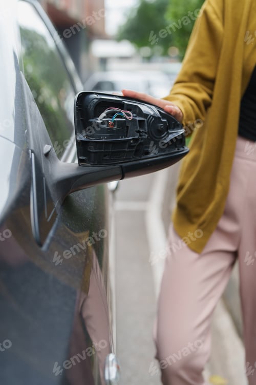 Preview: Person examining damaged car side mirror after collision