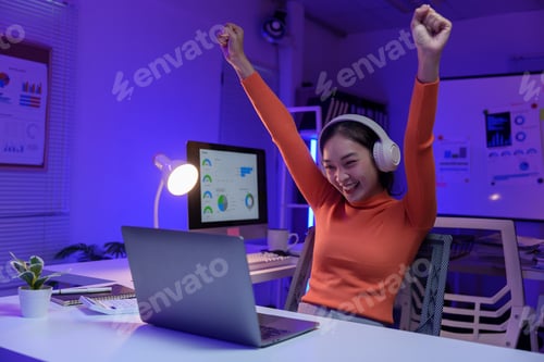Preview: Young professional raising arms and expressing joy while looking at laptop screen, celebrating succe