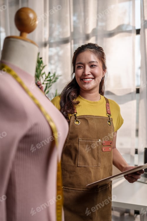 Preview: Asian woman business owner smiling designing garment