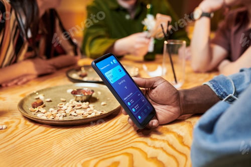 Preview: Black Man Making Mobile Payment While Dining with Friends