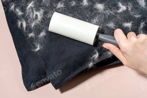 Preview: Hand holding a lint roller removing pet hair from a dark fabric surface, with visible lint and fiber