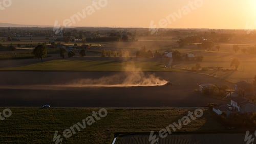 Preview: Farming tractor plowing dry agricultural field at sunset, creating dust plume in Po Valley, Italy, h