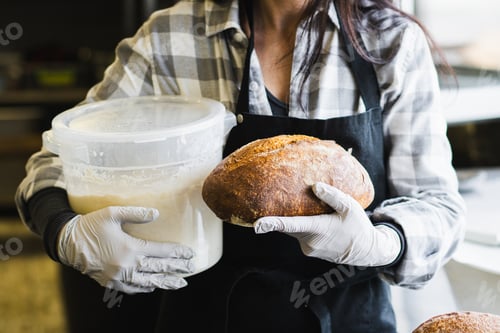 Preview: Smiling Female Baker Holding Fresh Artisan Sourdough Bread in Bakery