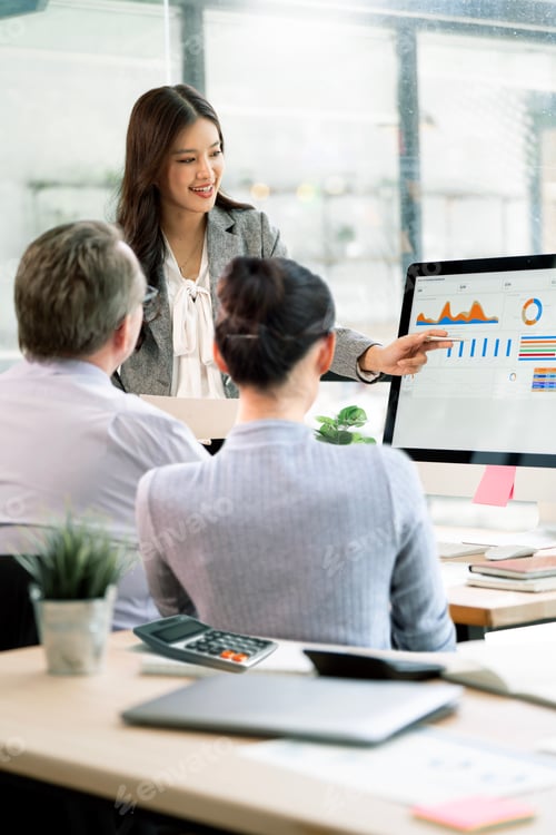 Preview: Asian Businesswoman Presenting Financial Data on Computer Screen to Team
