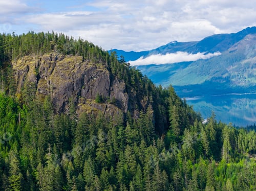 Preview: Rocky Cliff and Evergreen Forest Overlooking A Calm Mountain Lake in BC, Canada