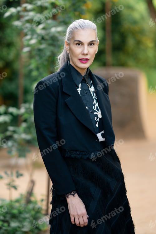 Preview: Poised lady dressed in dark clothes appears thoughtful among trees on peaceful pathway