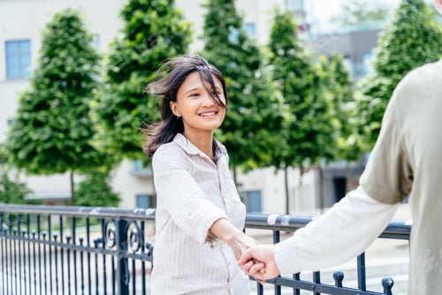 Preview: Close up portrait of smiling Asian woman holding hands with her partner on city bridge