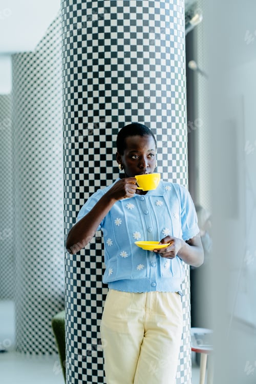 Preview: Black female designer holding coffee in modern creative office with geometric columns
