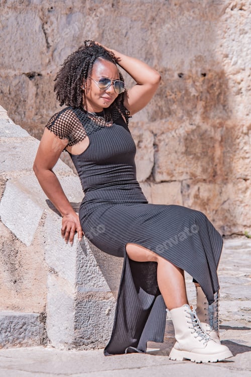 Preview: Stylish dark-skinned Hispanic woman in sunglasses poses on stone steps of an old town.