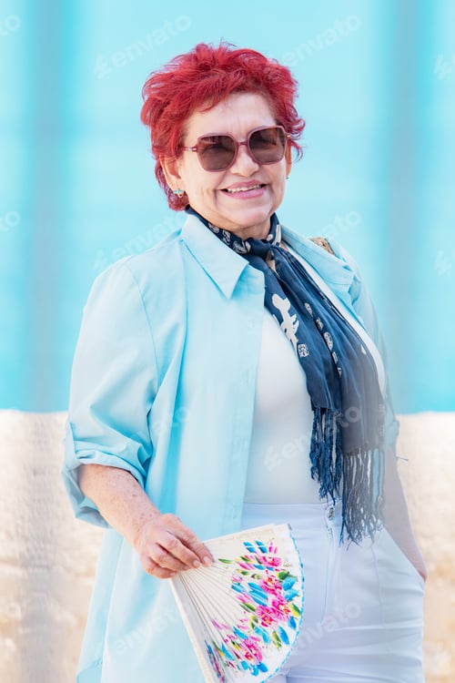 Preview: An elegantly dressed, attractive elderly woman holds a decorative fan, smiles