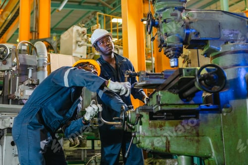 Preview: Two technicians in coveralls and hard hats operating a lathe machine in a factory