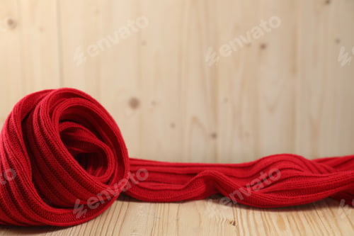Preview: Red knitted scarf on wooden table, space for text