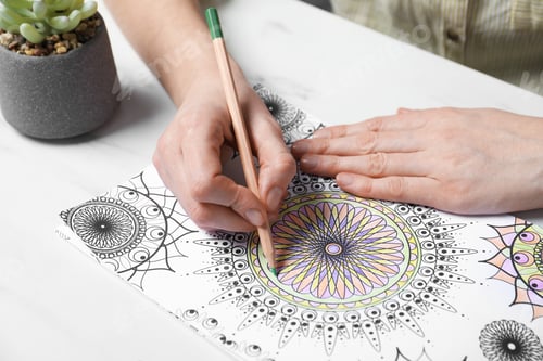 Preview: Woman coloring antistress picture with pencils at white table, closeup