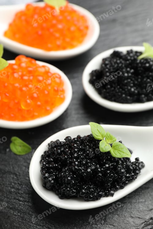 Preview: Delicious red and black caviar with basil in spoons on black board, closeup