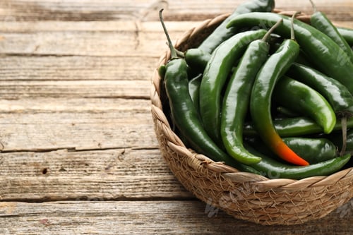 Preview: Fresh chili peppers in wicker basket on wooden table, closeup. Space for text