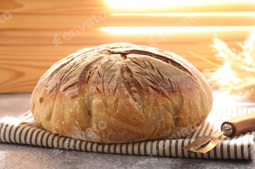 Preview: Loaf of freshly baked bread, lame and spikes on grey table, closeup