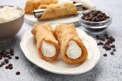 Preview: Delicious cannoli with cheese and chocolate chips on light grey table, closeup