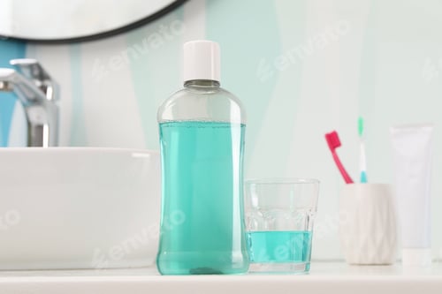 Preview: Bottle of mouthwash, toothbrushes and glass on white table in bathroom