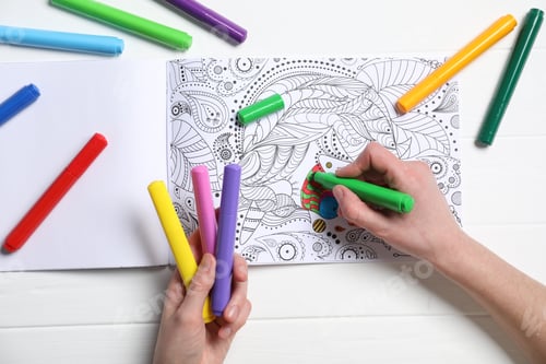 Preview: Woman coloring antistress picture with felt tip pen at white table, top view