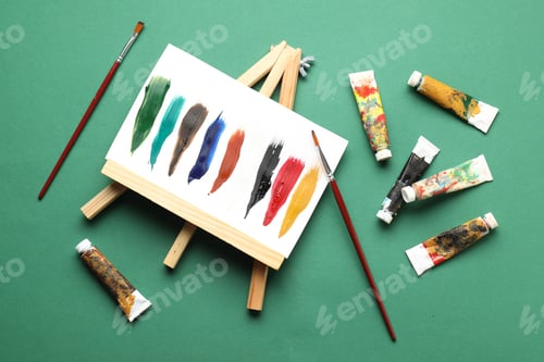 Preview: Tubes with watercolor paints, painting and brushes on green background, flat lay