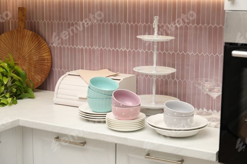 Preview: Set of clean plates, bowls, glasses and breadbox on white marble countertop in kitchen