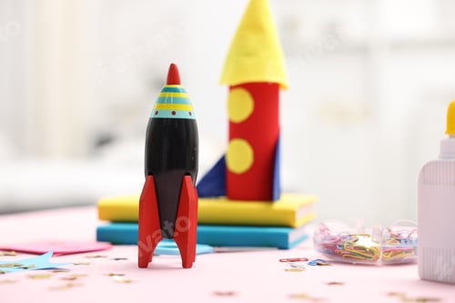Preview: Toy and handmade rockets on light pink table indoors, closeup