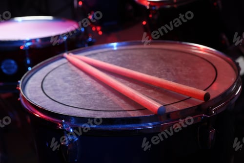 Preview: Wooden drumsticks on drum in color light, closeup