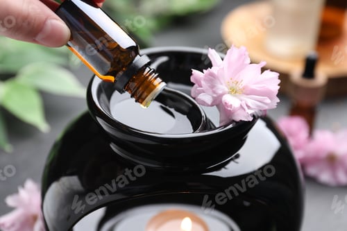 Preview: Aromatherapy. Woman dripping essential oil into aroma lamp at black table, closeup