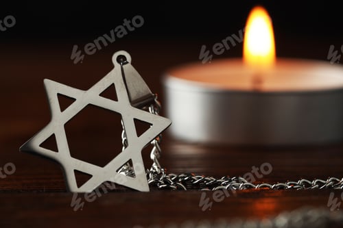 Preview: Holocaust Remembrance Day. Pendant in shape of Star of David and burning candle on wooden table agai