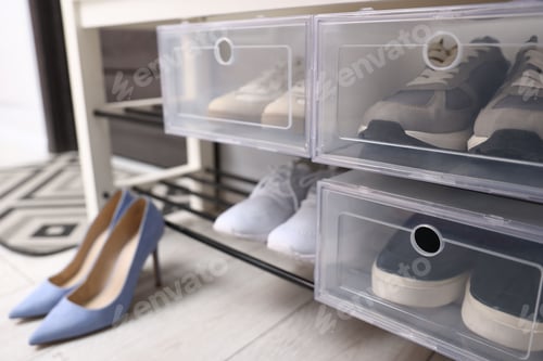 Preview: Bench with footwear in boxes and pair of stylish high-heeled shoes on floor indoors, selective focus