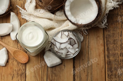 Preview: Delicious coconut yogurt in glass jar, flakes and fruits on wooden table, flat lay. Space for text
