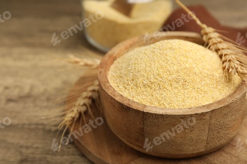 Preview: Raw semolina in bowl with spikes on wooden table, closeup. Space for text