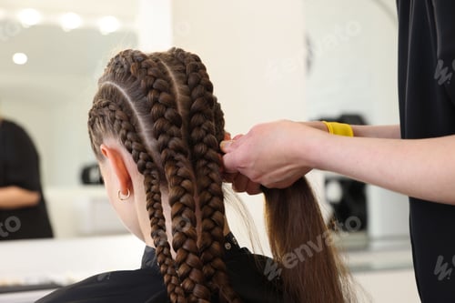Preview: Hairstylist braiding teenage girl's hair in salon, closeup