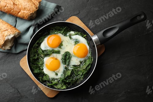 Preview: Fried eggs with spinach in frying pan and bread on black table, flat lay