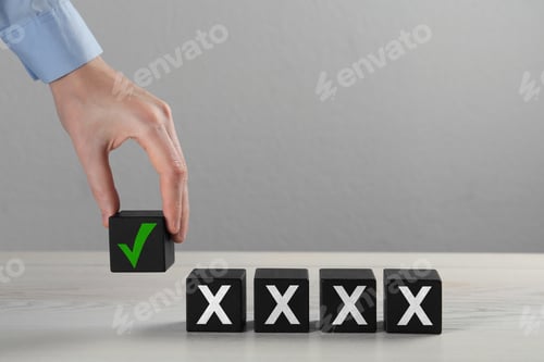 Preview: Woman putting wooden cube with checkmark next to others with cross marks on table, closeup. Followin