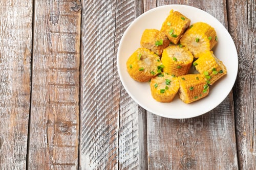 Preview: Pieces of boiled corn cobs with green onion on wooden table, top view. Space for text
