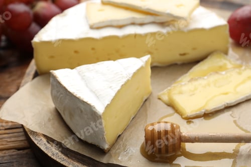 Preview: Slices of delicious brie cheese, grapes, honey and dipper on wooden table, closeup