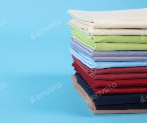 Preview: Stack of colorful bed linens on light blue background, closeup. Space for text