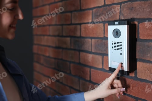 Preview: Woman pressing button on intercom panel near brick wall, closeup