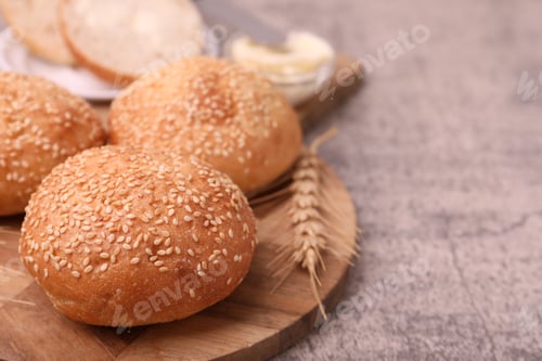 Preview: Yummy buns with sesame seeds and wheat ear on grey table, closeup. Space for text